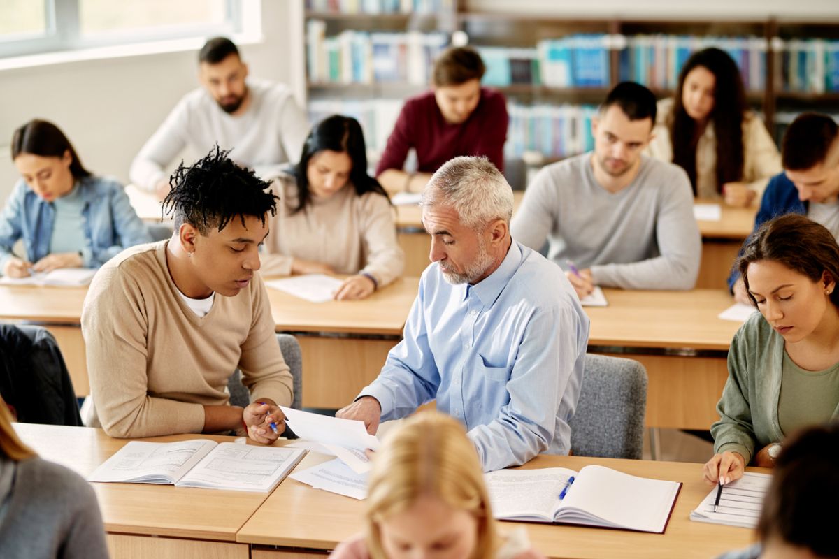 Young African American student talking to his professor who is assisting him with the lecture in the classroom.