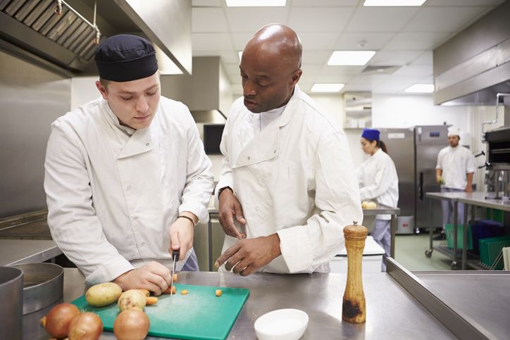 Chef training the sous chef in a restaurant kitchen or culinary school.